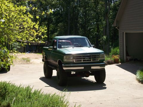 1992 Ford Bronco - Green lifted 1992 Ford Bronco parked in a driveway with trees and a garage in the background.