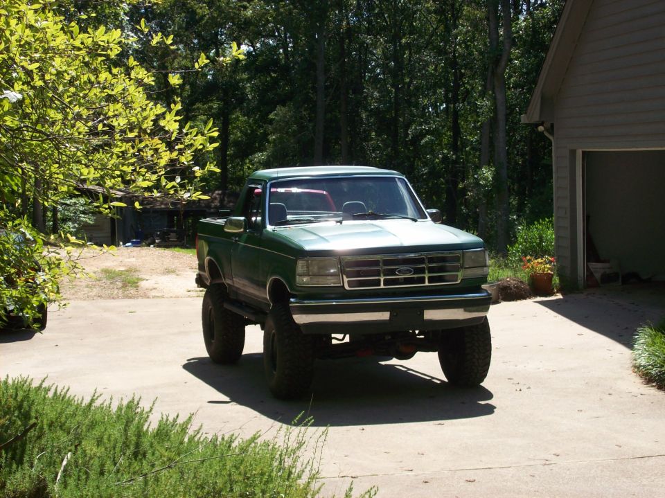 Lifted green Ford Bronco with top removed parked on driveway, front three-quarter view