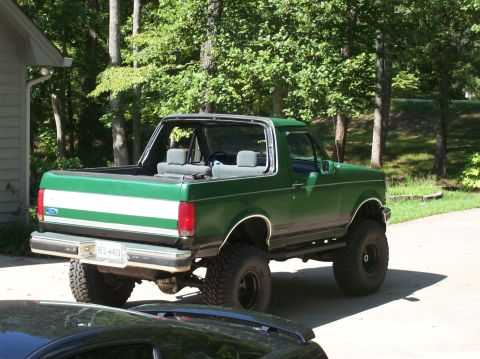 1992 Ford Bronco - This lifted green Ford Bronco is parked in a driveway with trees in the background.