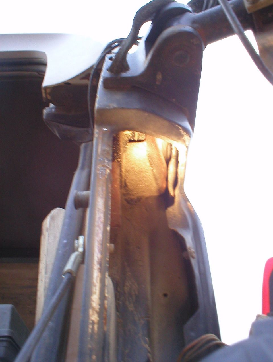 Underside view of a vehicle's frame rail and body mount with sunlight on rusty bracket