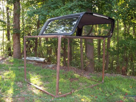 1992 Ford Bronco - A car top is displayed on a metal frame in a wooded area.