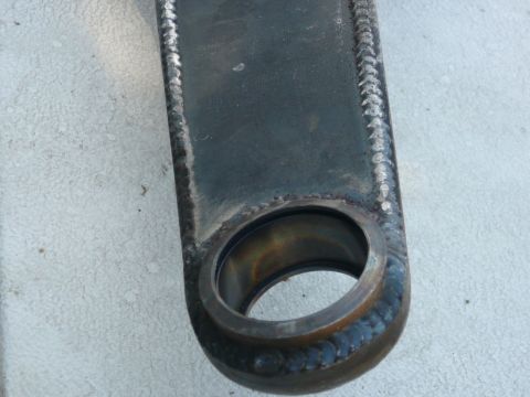 1988 Ford Bronco - Close-up of a metal suspension component, showing detailed welds and a central circular opening. The part is resting on a textured surface.