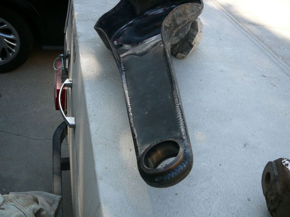 Close-up of a heavy, welded metal component resting on a concrete surface. Another metal piece is visible to the right