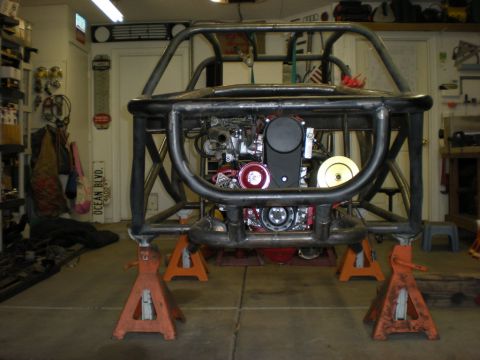 Suzuki Samurai - A custom off-road vehicle chassis is supported by jack stands in a garage, revealing its engine and roll cage.