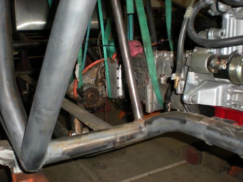 Suzuki Samurai - Drivetrain being trial-fitted into a bare-metal tube chassis, with the transmission and transfer case slung from green ratchet straps while…