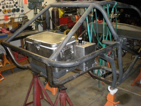 Suzuki Samurai - Rear corner of a bare tube-chassis buggy under construction on red and orange stands in a home shop, with a polished aluminum storage box a…