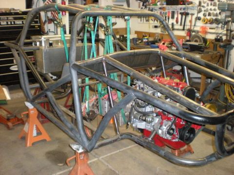 Suzuki Samurai - A bare tube-frame buggy chassis with full roll cage, suspended from ratchet straps and resting on orange jack stands in a home workshop. An…