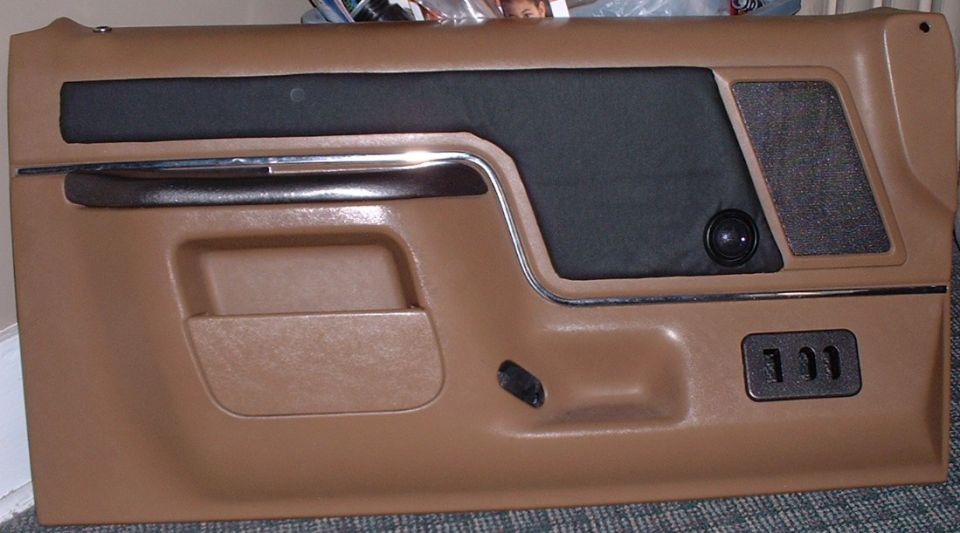 Brown car door panel with black fabric insert, chrome trim, and speaker grille