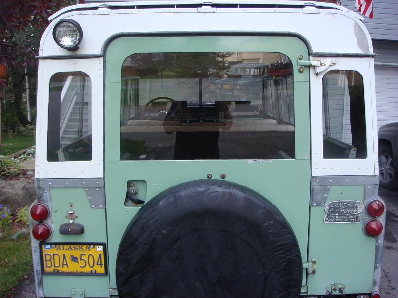 Rear of white/green Land Rover Series with black spare cover and Alaska plate BDA 504