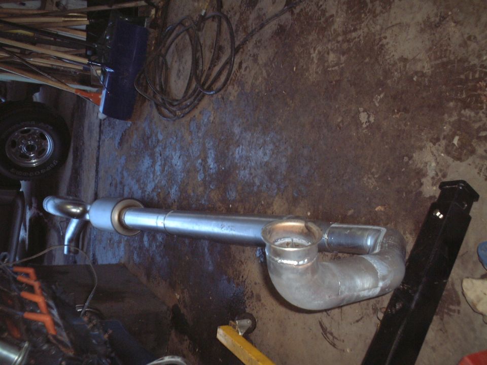 Custom welded exhaust pipe with elbow, muffler and turndown tip lying on a garage floor