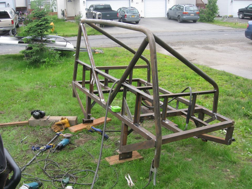Metal frame for a custom roll cage, with tools like grinders and gloves nearby