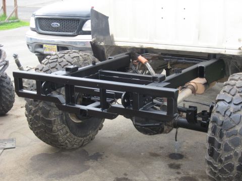 1990 Ford F-250 - The front of a Ford F-150 is visible behind a custom truck chassis with large off-road tires.