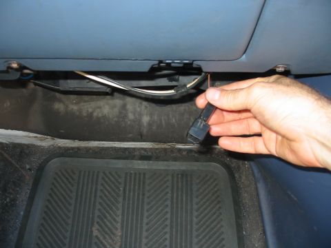 1992 Ford Bronco - A hand disconnects a wiring harness connector from the underside of a vehicle's dashboard.