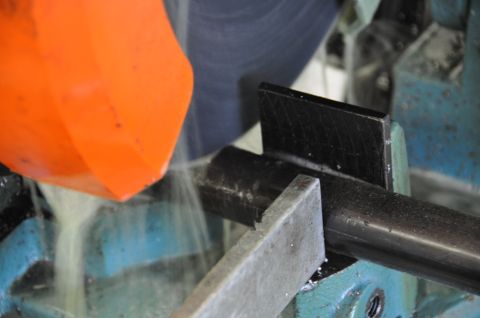 1996 Ford Bronco - A metal pipe is being cut by a band saw, with coolant being applied to the blade.