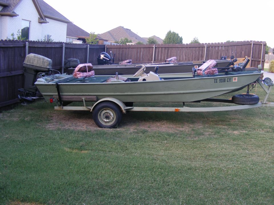 Two green boats on trailers parked on grass in a backyard. One boat has TX 9058 CW license plate