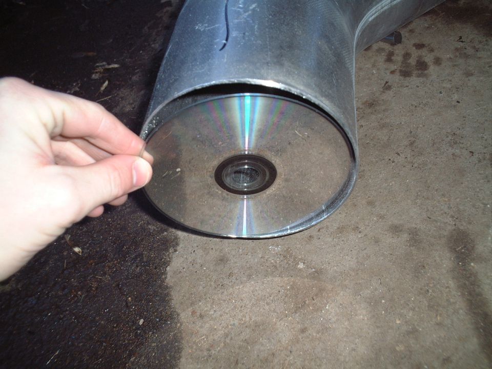 Hand holding a CD against the end of a large metal cylinder on concrete floor