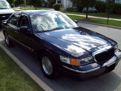 1999 Mercury Grand Marquis - A dark blue 1999 Mercury Grand Marquis is parked on a residential street with a white van visible to the left.