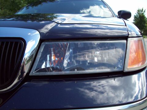 1999 Mercury Grand Marquis - The front corner of a dark sedan, showing the headlight and chrome grille details.