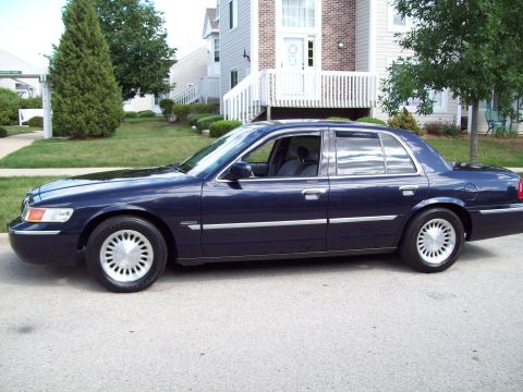 1999 Mercury Grand Marquis - A dark blue sedan is parked on a street in front of a residential building.