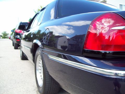 1999 Mercury Grand Marquis - A dark blue 1999 Mercury Grand Marquis is parked in a line of cars, showing its rear quarter panel and taillight.