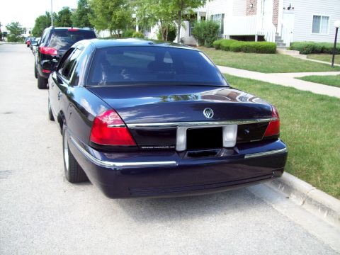 1999 Mercury Grand Marquis - The rear of a dark blue sedan is visible, parked on a residential street next to a curb.