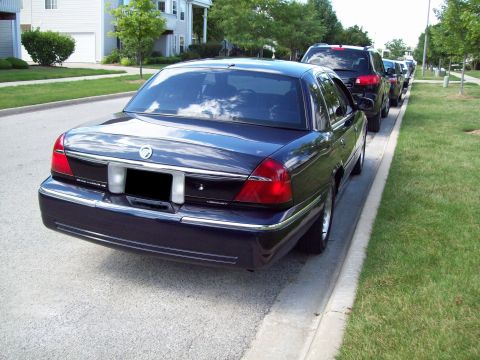 1999 Mercury Grand Marquis - A dark blue sedan is parked on the side of a residential street, with other vehicles behind it.