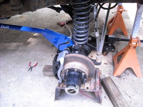 1979 Ford F-150 - Close-up of a truck's front suspension and brake system, supported by jack stands and a blue aftermarket arm.