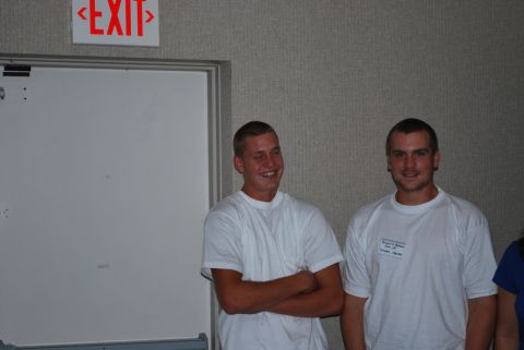 1996 Ford Bronco - Two men in white t-shirts stand in front of a textured wall and a whiteboard, with an EXIT sign overhead.