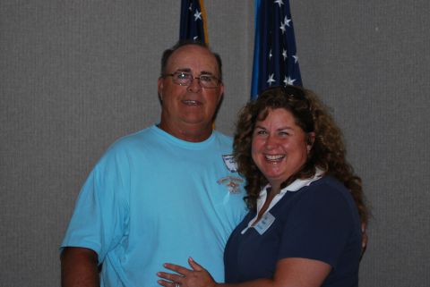 1996 Ford Bronco - A couple poses for a photo in front of two flags, with the man wearing a light blue t-shirt and the woman in a dark blue shirt.