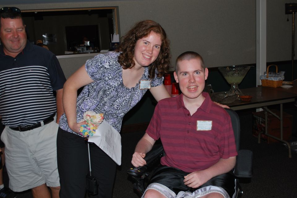 Man in striped shirt, woman in patterned shirt, and man in wheelchair at an indoor event