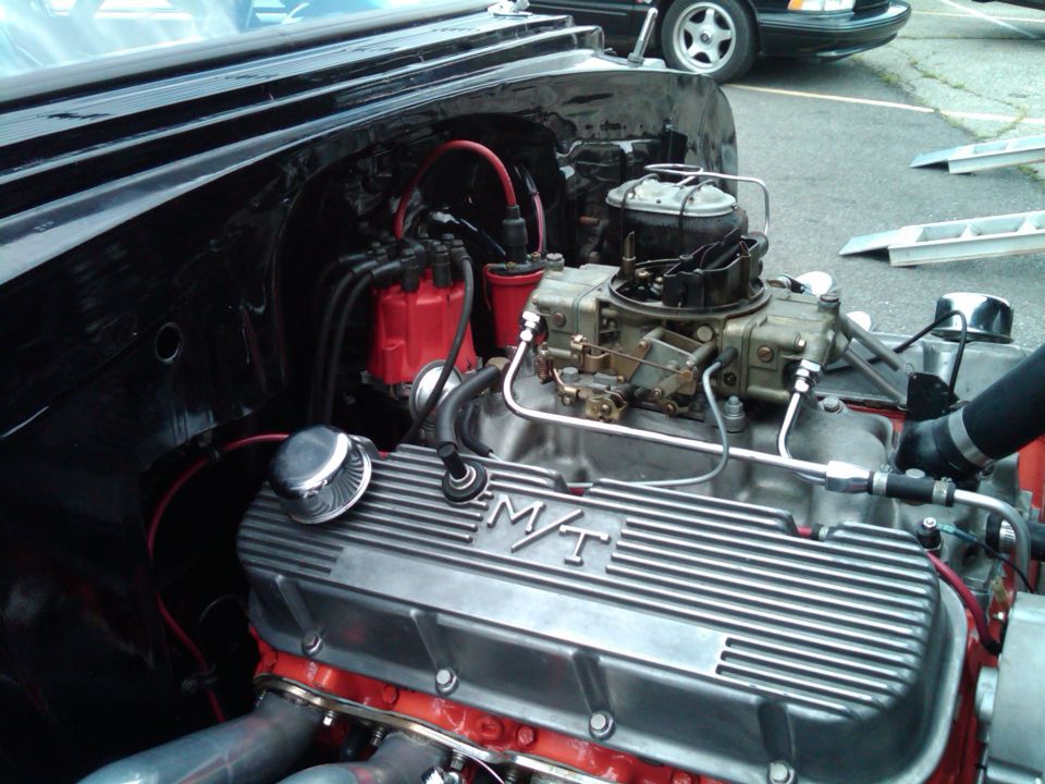 Red V8 with finned M/T valve covers and carburetor in a black car's engine bay