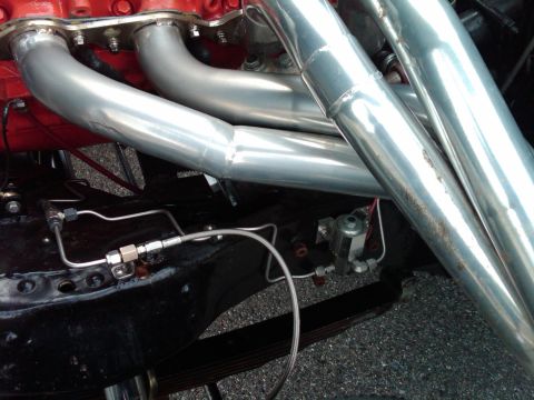 1955 Chevrolet Bel Air - Shiny chrome exhaust headers and fuel lines are visible on the engine of a vehicle.