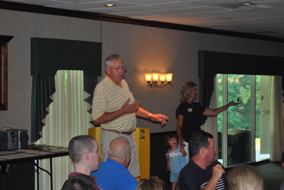 People gathered indoors, with a man speaking and a woman gesturing near a window