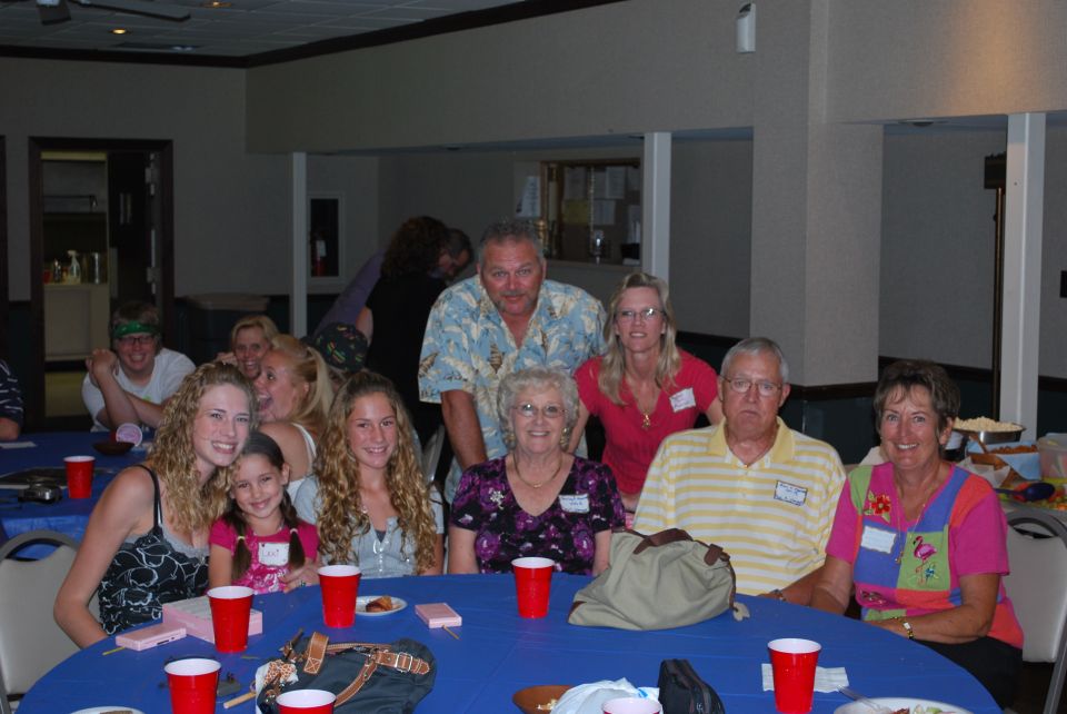 Group of people, including young women and older adults, seated at blue tables with red cups