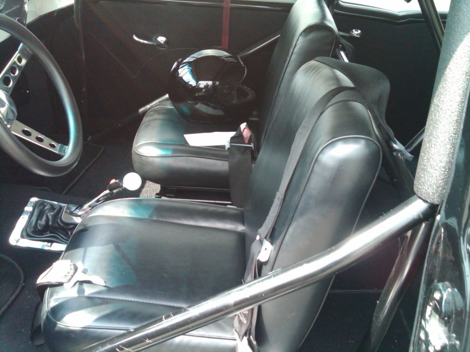 Interior view of a car with black racing seats, a roll cage, a racing helmet on the passenger seat, and a manual shifter