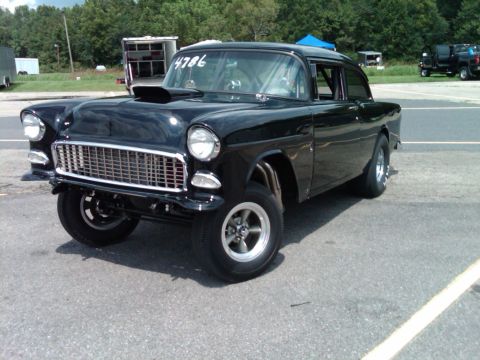 1955 Chevrolet Bel Air - A modified 1955 Chevrolet with a prominent hood scoop sits on a paved surface, likely a drag strip.