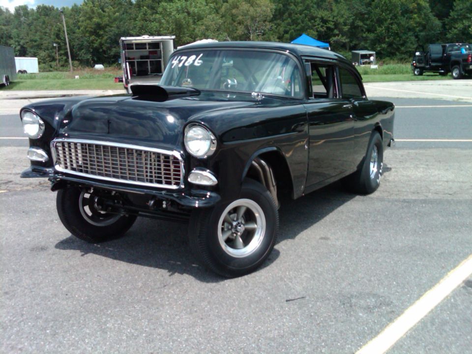 Black 1955 Chevrolet gasser drag car with hood scoop in a track staging lot