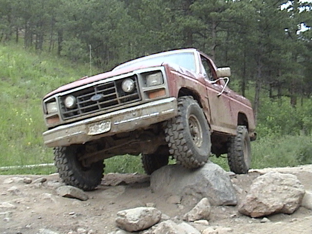 Faded red 1980s Ford pickup crawling over boulders on a rocky trail