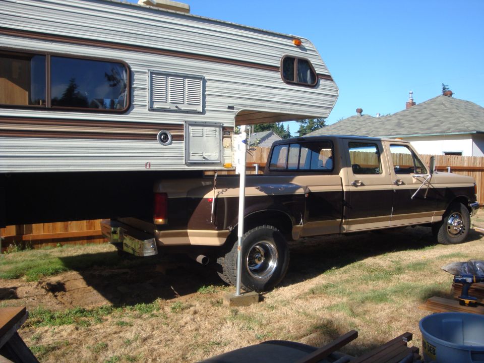 Ford pickup truck with a camper shell in a backyard. The truck is brown and tan