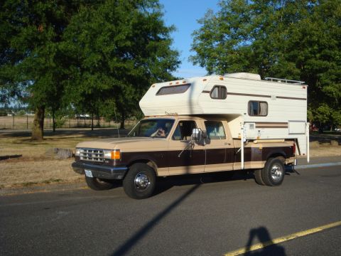 1988 Ford F-350 - This two-tone Ford pickup truck is equipped with a camper shell, suggesting it's set up for travel or camping.