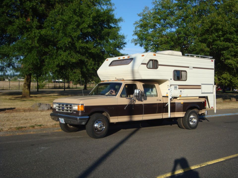 Ford pickup truck with camper shell, two-tone brown and tan, driving on a road