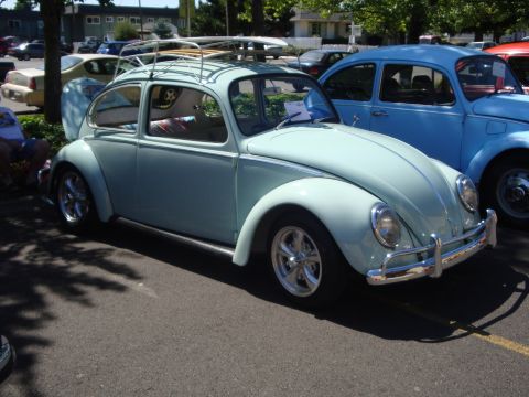1964 Ford Fairlane - A light blue Volkswagen Beetle is parked at an outdoor car show, with another blue Beetle beside it.
