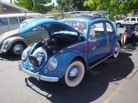 1964 Ford Fairlane - A blue Volkswagen Beetle is parked outside with its hood open, revealing the spare tire and engine compartment.