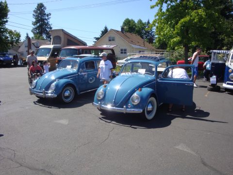 1964 Ford Fairlane - Two blue Volkswagen Beetles are displayed at an outdoor event, with one having its driver's side door ajar.