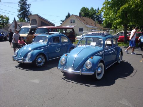 1964 Ford Fairlane - Two classic blue Volkswagen Beetles are displayed at an outdoor show, with one a roof rack.
