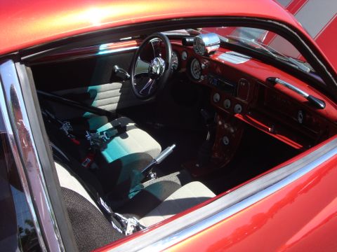 1964 Ford Fairlane - The interior of a red car features racing seats, a roll cage, and aftermarket gauges, suggesting a performance build.