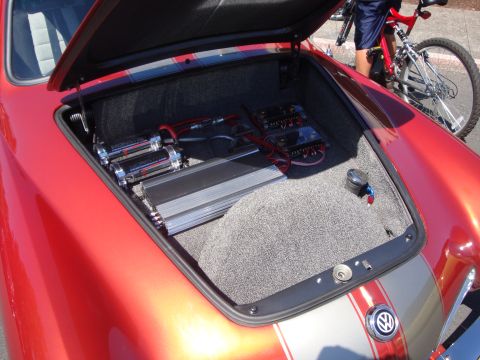 1964 Ford Fairlane - The trunk of a red car is open, revealing custom audio equipment and air ride components. A Volkswagen emblem is visible.