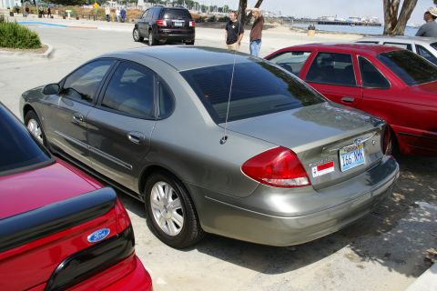 1990 Ford Taurus - A gray sedan is parked outdoors, with a red car to its left and another vehicle behind it.