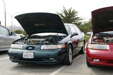 1990 Ford Taurus - Two Ford Taurus SHO models are parked side-by-side with hoods open, revealing their engines.