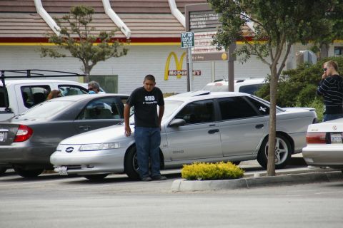 1990 Ford Taurus - A silver sedan, possibly a 1990 Ford Taurus SHO, is parked in a lot with a man standing beside it.